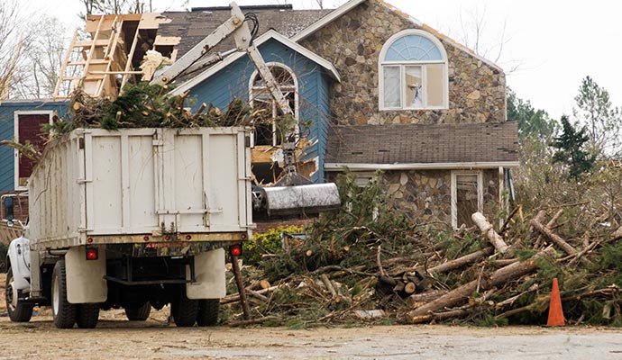 Heavy machinery loading storm debris into a dump truck at a residential property