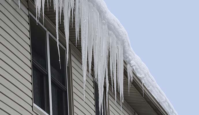 Icicles hanging heavily from the gutter and roofline of a residential building