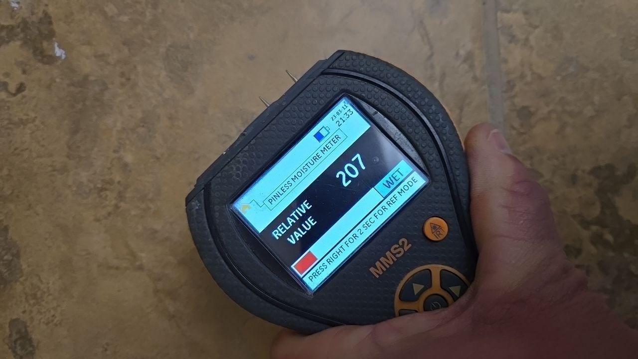 A pinless moisture meter displaying a 'WET' reading with a relative value of 207, confirming significant moisture levels in the affected area.
