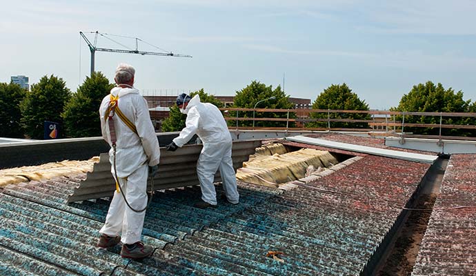Two people are removing asbestos from roof
